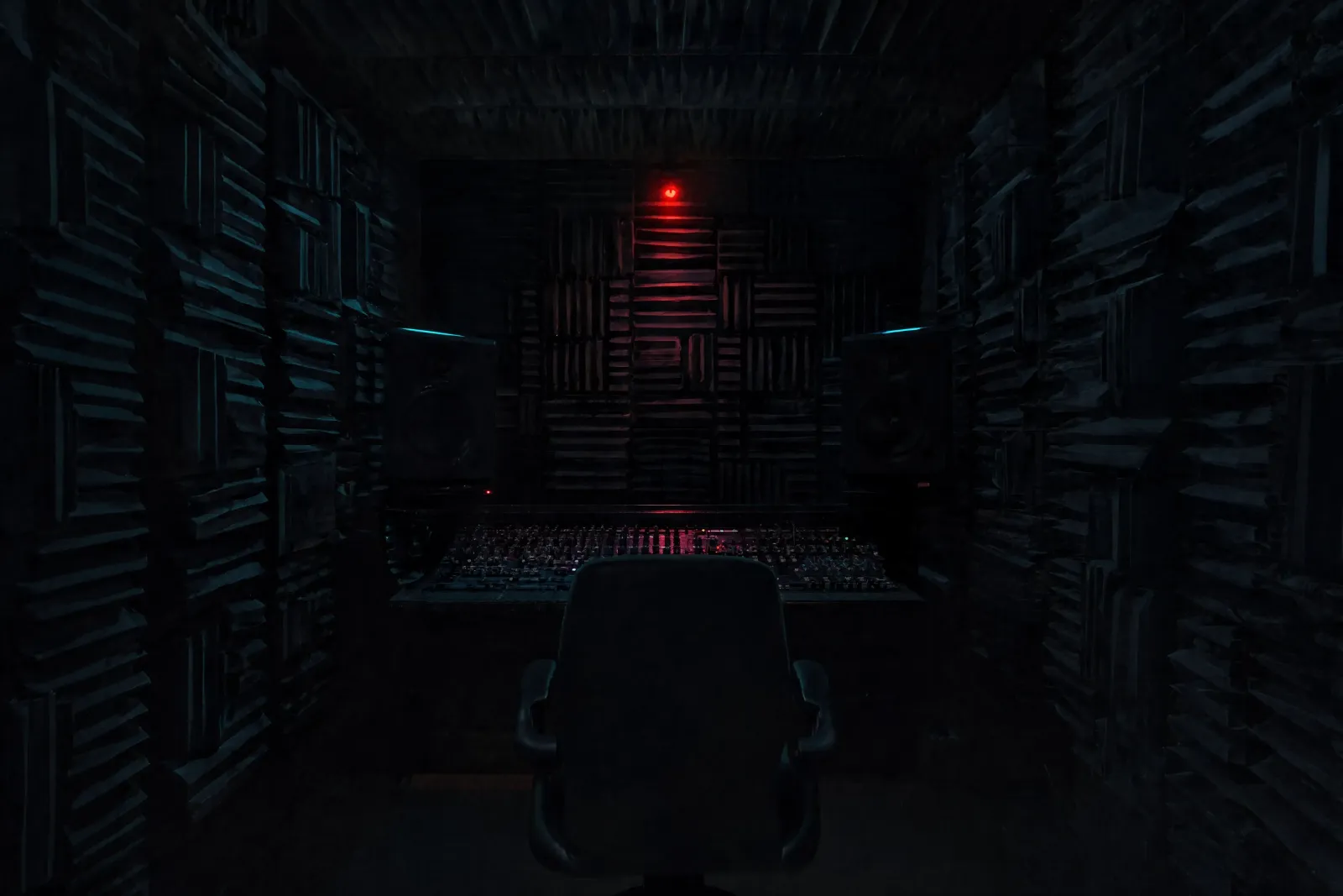 A small room lined with acoustic foam, a mixing desk and a chair facing a single red light